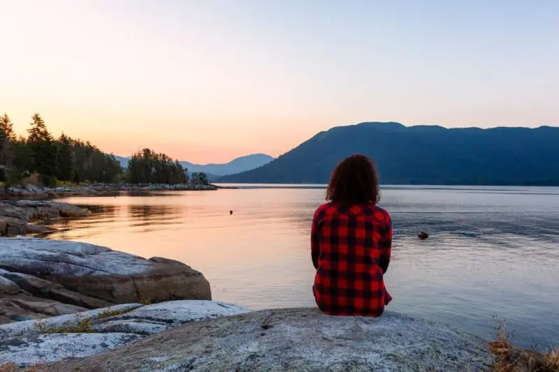 Woman sat by lake at sunset